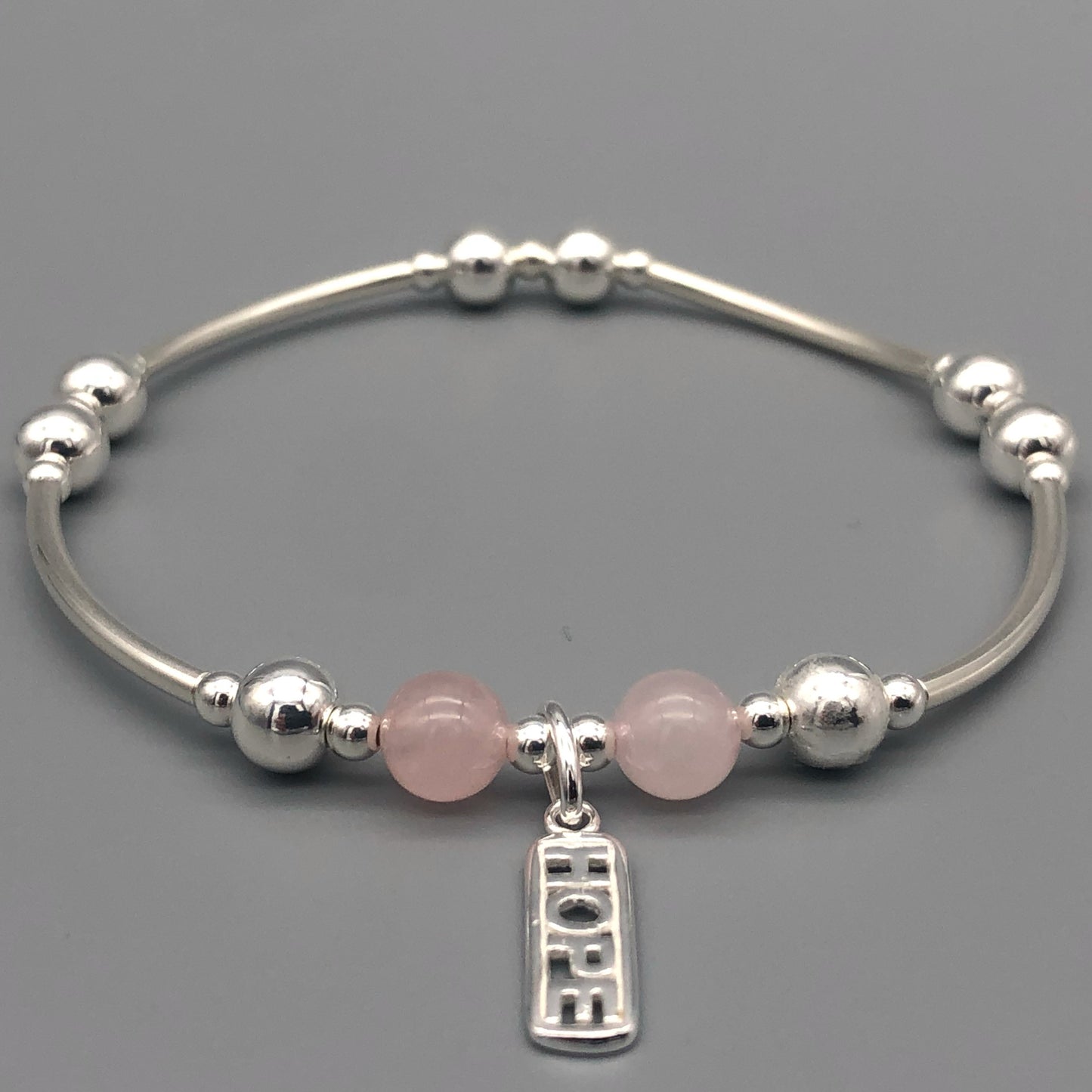 Closeup of "Hope" rose quartz healing crystal women's silver stacking charm bracelet by My Silver Wish