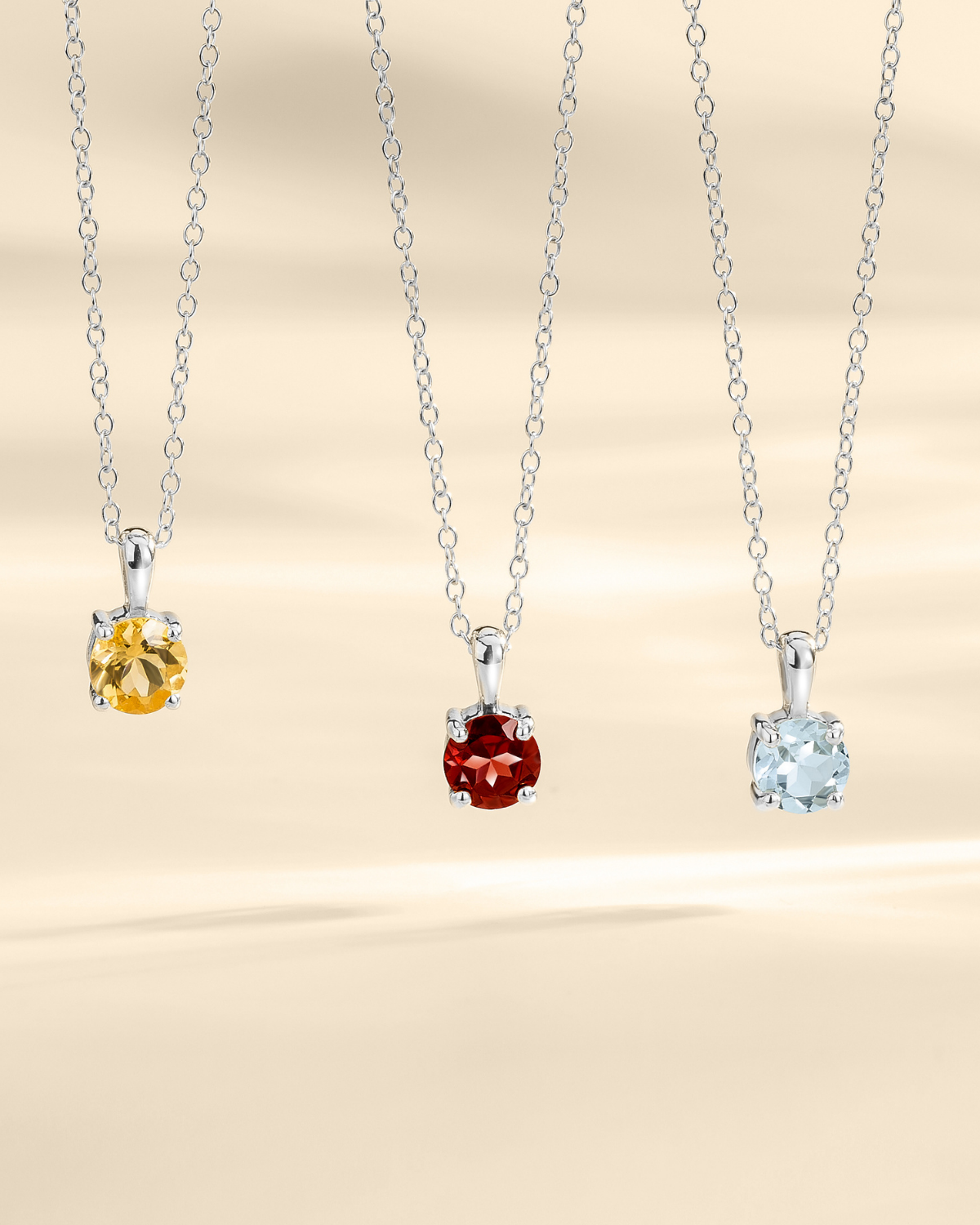 Three silver pendants with different colored gemstones on a beige background