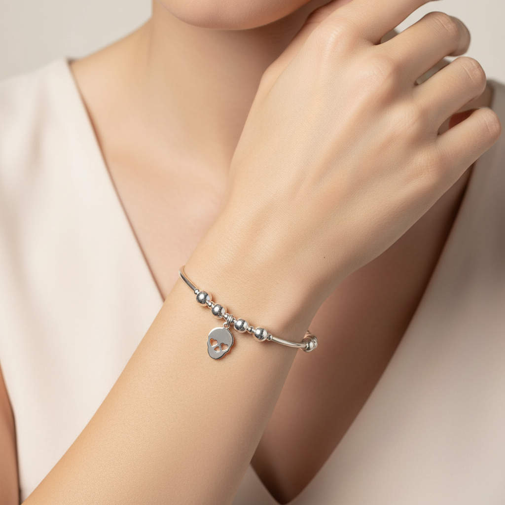 Silver stacking bracelet with a heart charm on a wrist against a neutral background